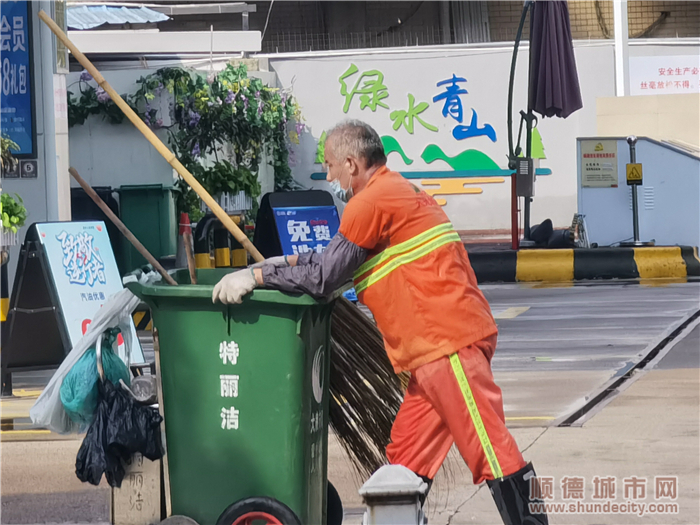 环卫工人吴伯身穿橙黄色工作服,推着一个大垃圾桶,沿新宁路清扫垃圾.