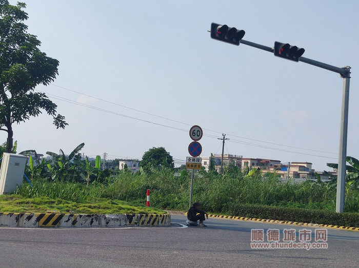 一名流浪老人难顶烈日曝晒，正蹲坐在均安新均榄路新华段公路十字路口花基旁。（均安镇公共服务办公室供图）_副本.jpg